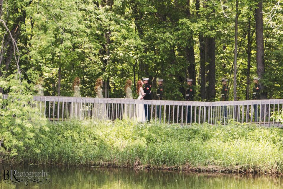 Wedding scene featuring a bride, groom, and bridal party crossing a rustic wooden bridge