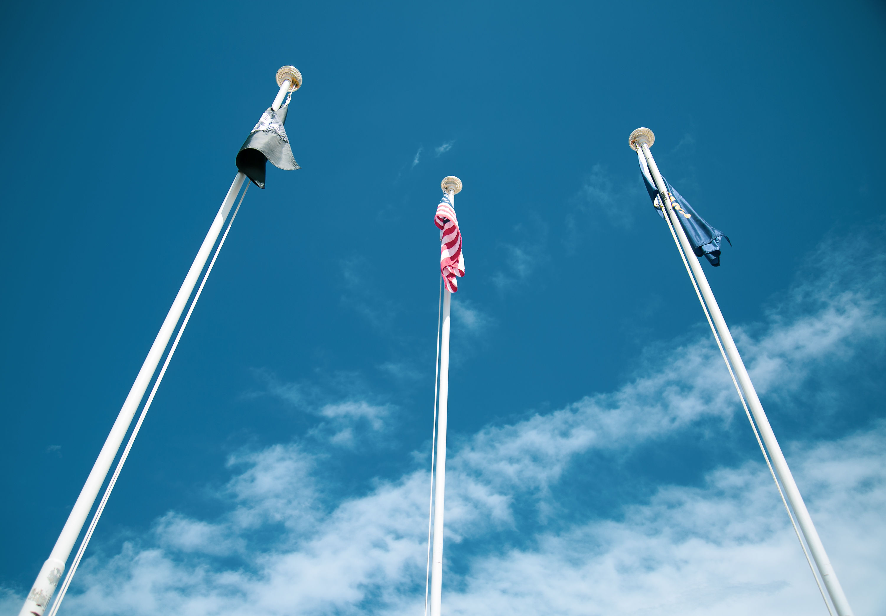 Three tall flagpoles with U.S. flags against a blue sky and scattered clouds.