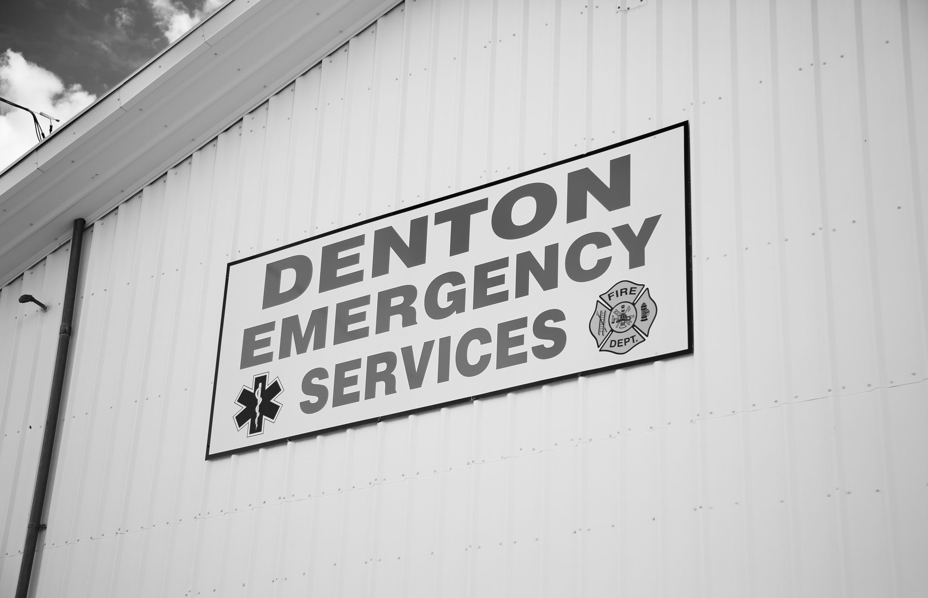Black-and-white wall sign: “DENTON EMERGENCY SERVICES” with a fire department emblem and medical cross.