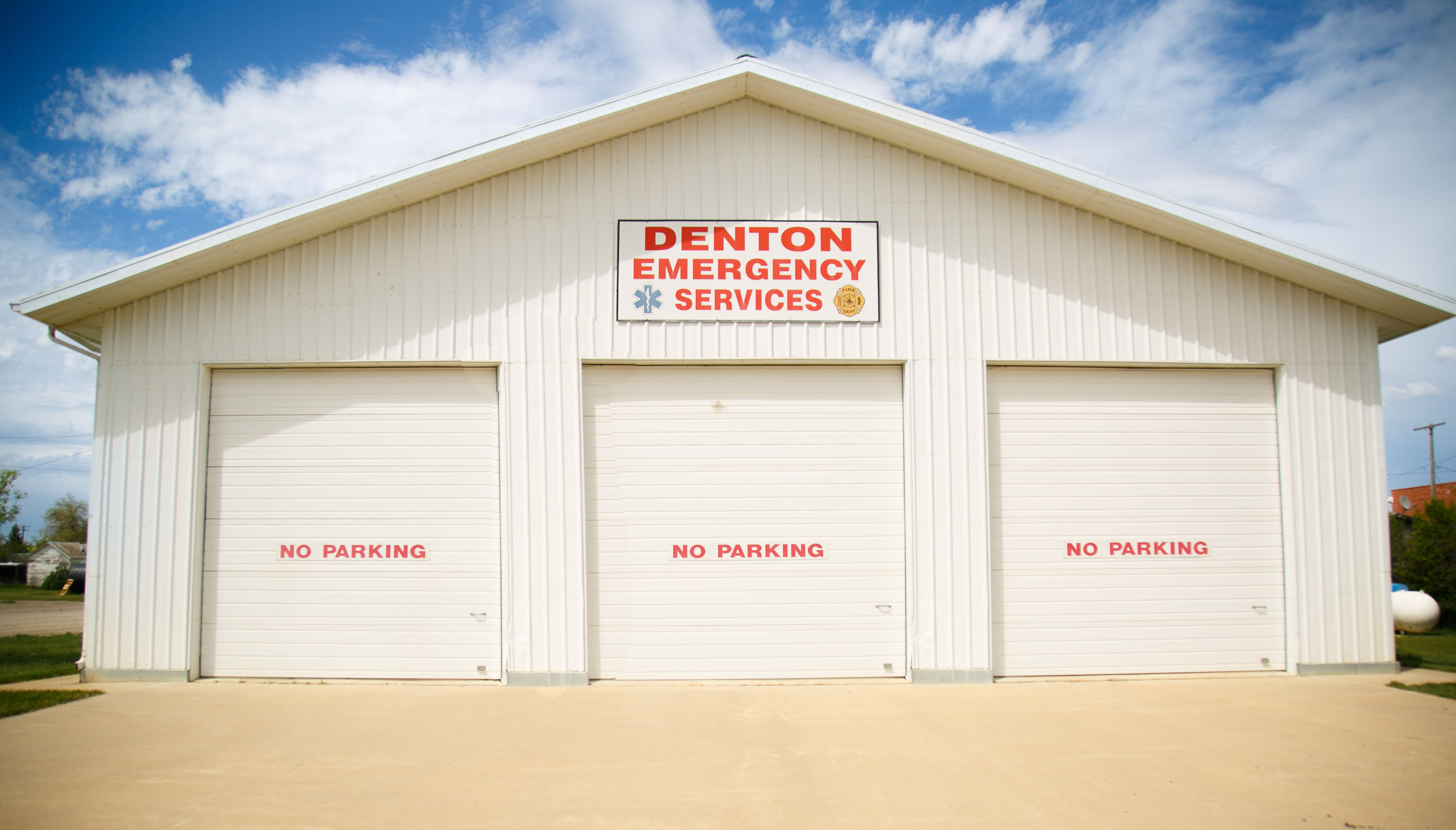 Denton Emergency Services building with three closed garage doors; red “NO PARKING” signs on each.