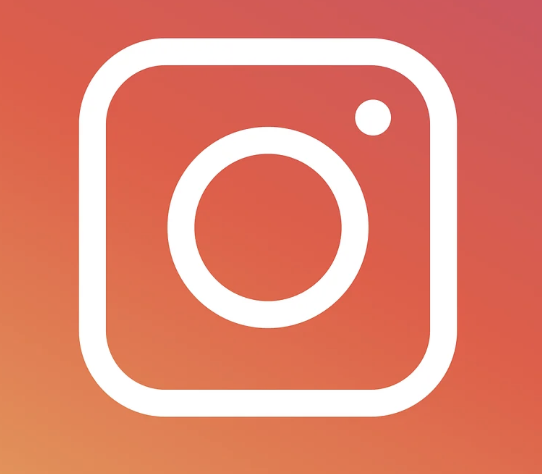 White camera icon with a circular lens outline inside rounded square on a red gradient background.