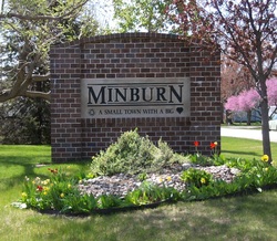 Brick sign reading “MINBURN” with smaller text below, surrounded by flowers and shrubs.