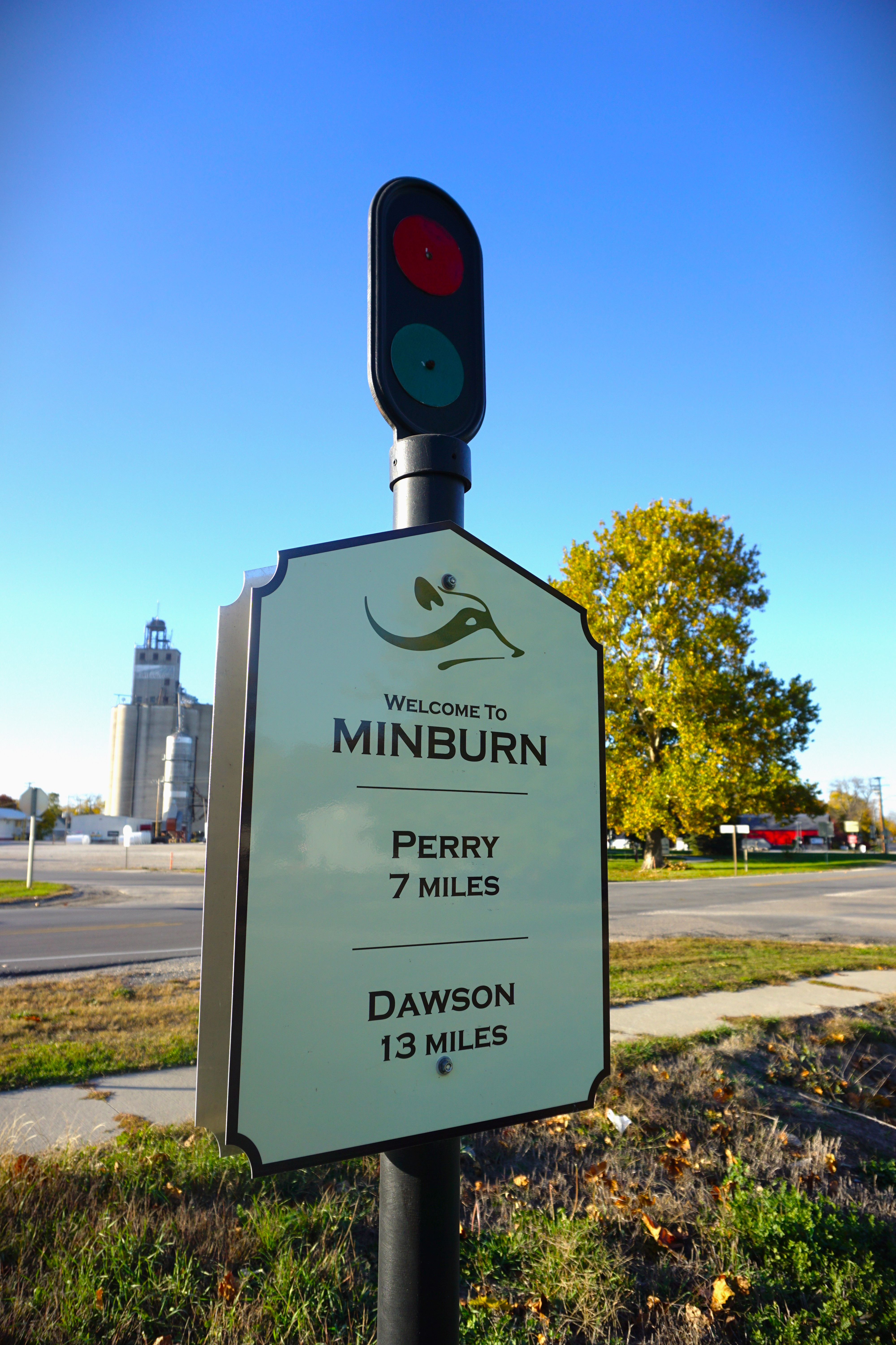Green roadside sign: “Welcome to Minburn,” “Perry 7 Miles,” and “Dawson 13 Miles,” with a small logo above.