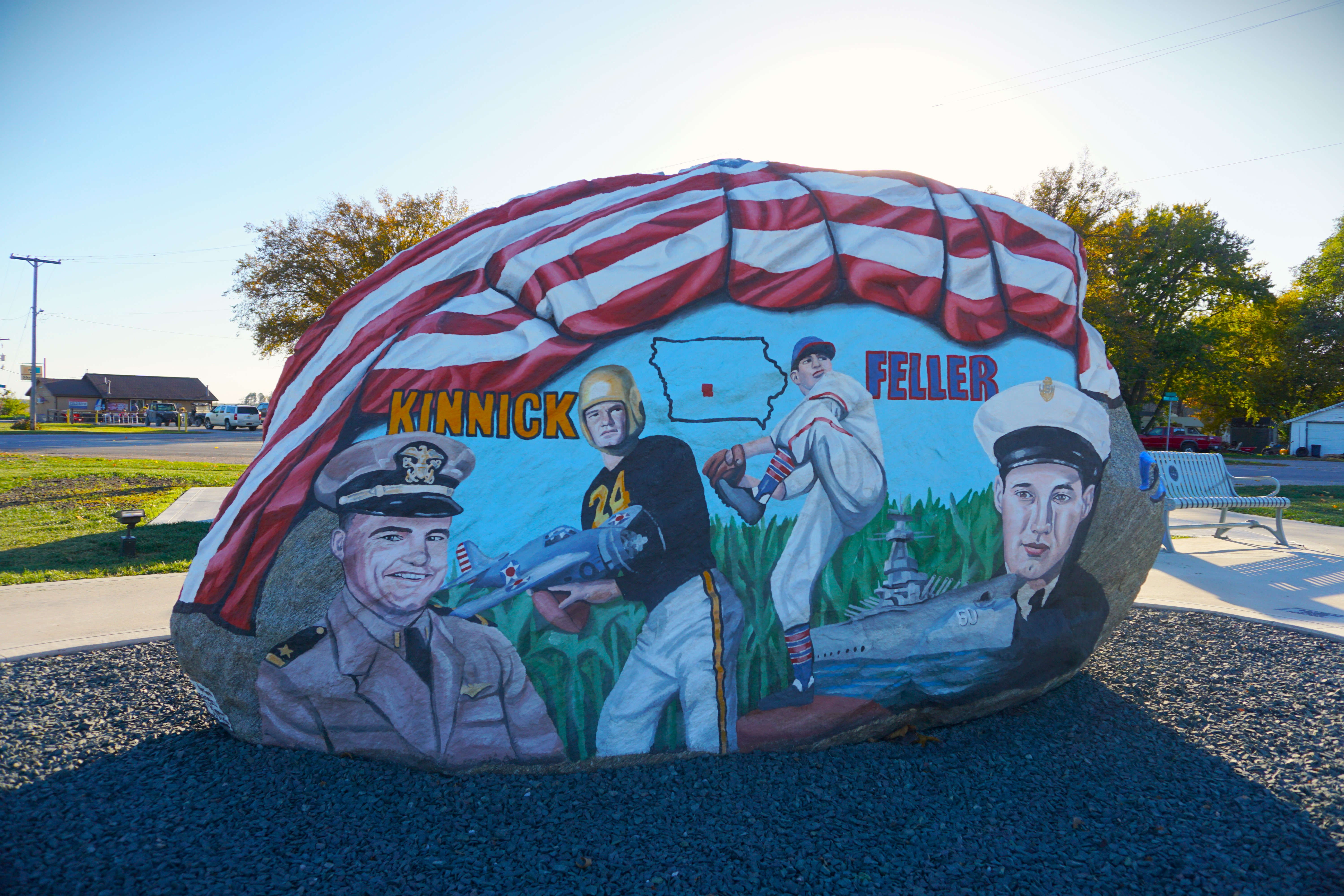 Painted mural on a stone boulder showing soldiers, red-and-white stars, and text “KINNICK” and “FELLER,” outdoors.