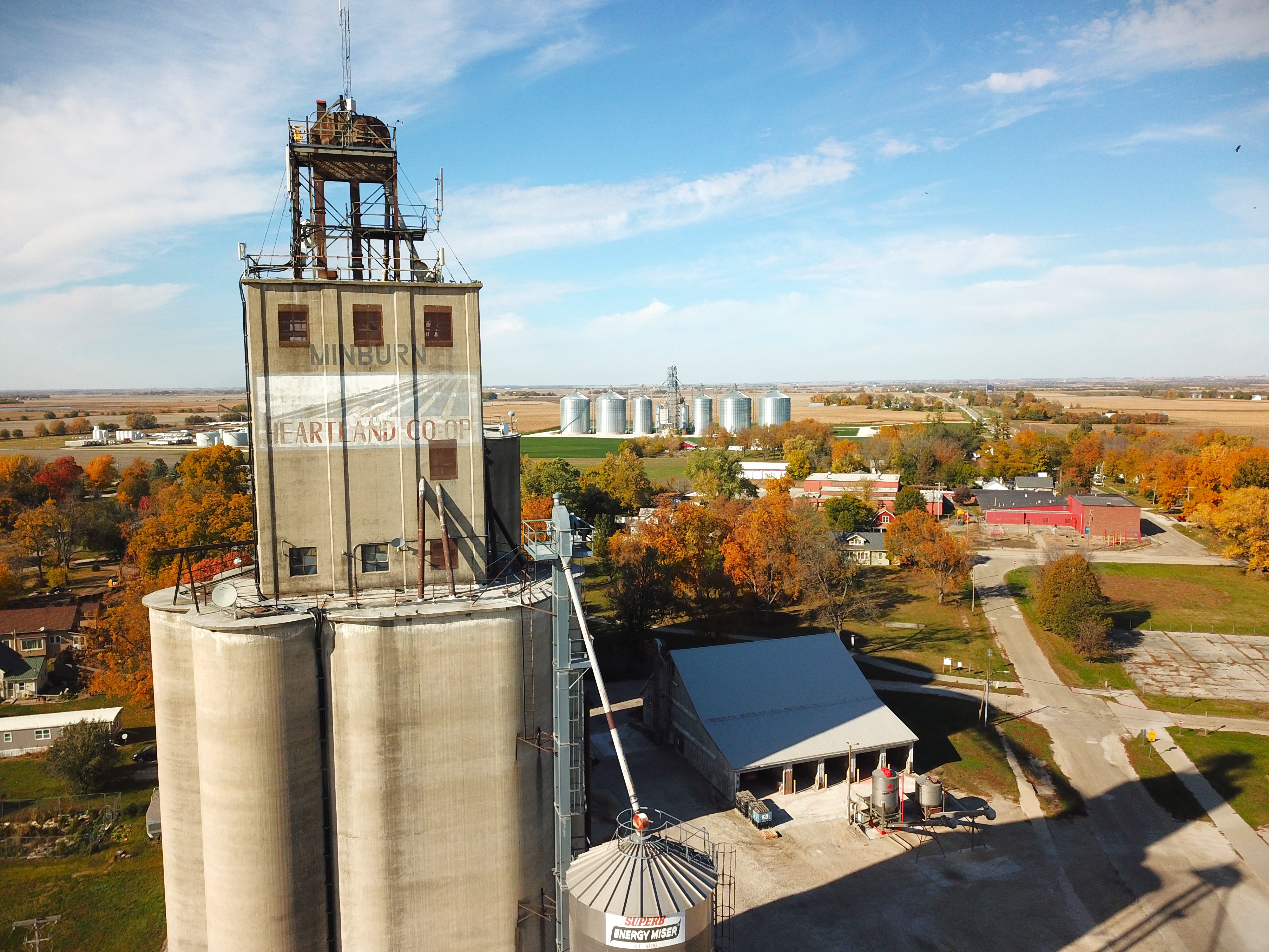 Aerial view of a grain/processing facility with “MINBURN” on a tower and “EARTHLAND COOP” on a building, surrounded by silos.