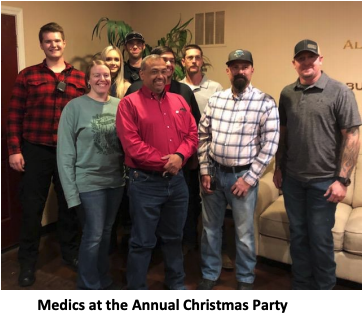 Group of medics posing together at an annual Christmas party indoors; caption reads “Medics at the Annual Christmas Party.”