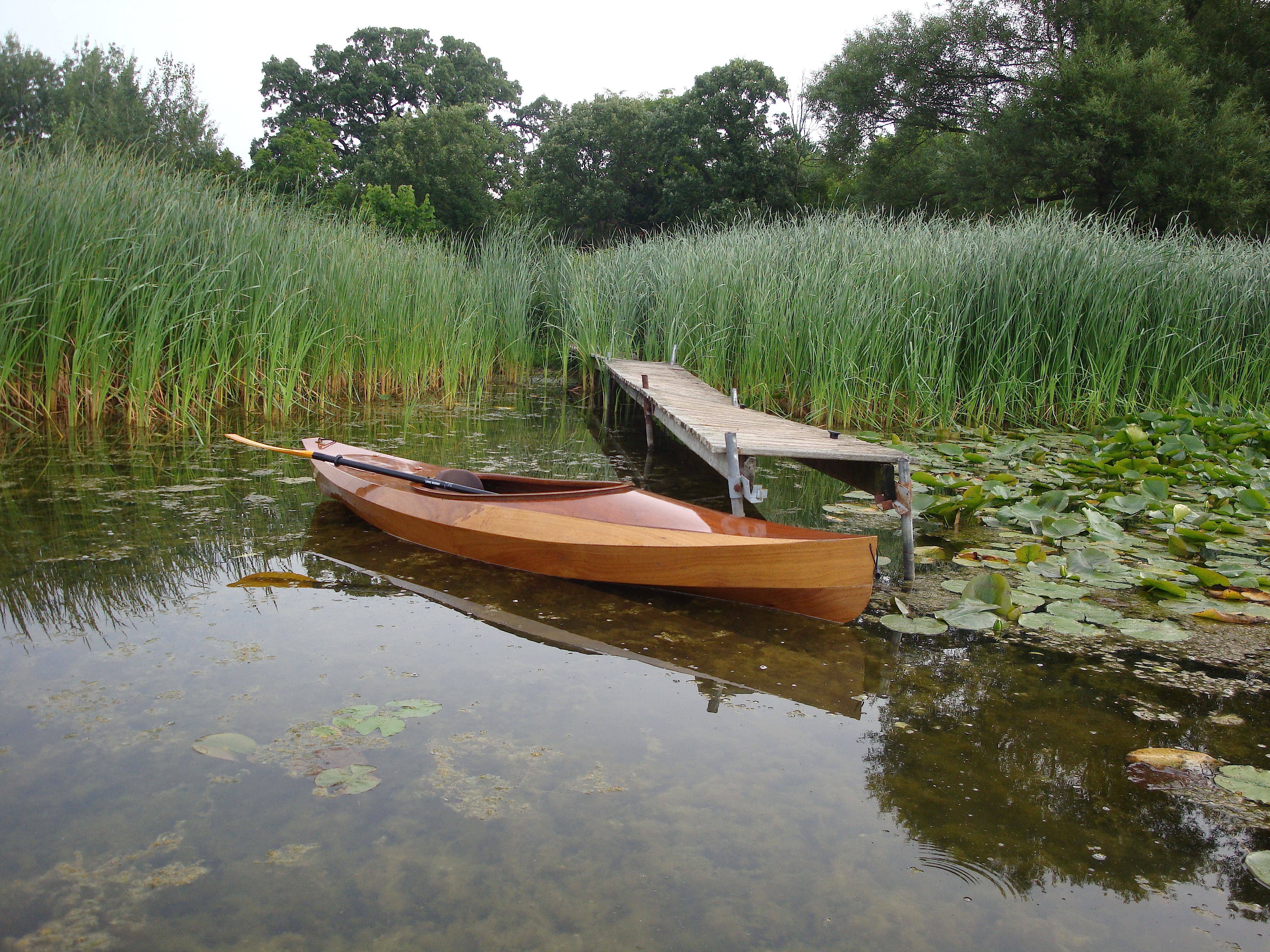 Wooden stitch-and-glue recreational kayak resting in shallow water near a dock