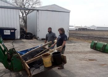 Road employees loading materials into the bucket of a green tractor loader