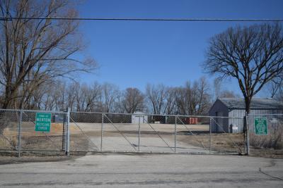 Fenced property with gates and green warning signs; leafless trees and clear blue sky.