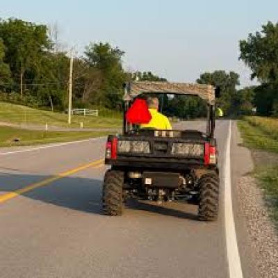 Pickup truck with rugged tires on a road, hauling a large sign frame with red and yellow panels.