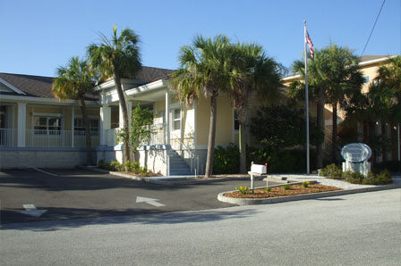 Building entrance with palm trees and a U.S. flag on a flagpole near a paved driveway.